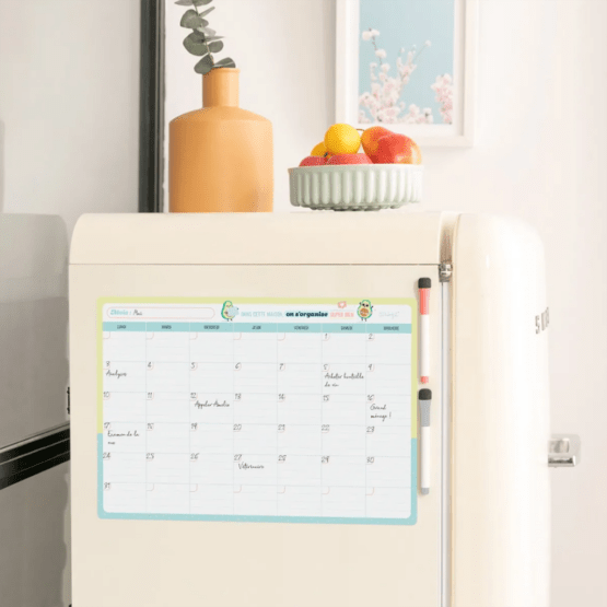 un tableau magnétique avec un planning mensuel, vue de face fixé sur un frigo sur un fond décoré
