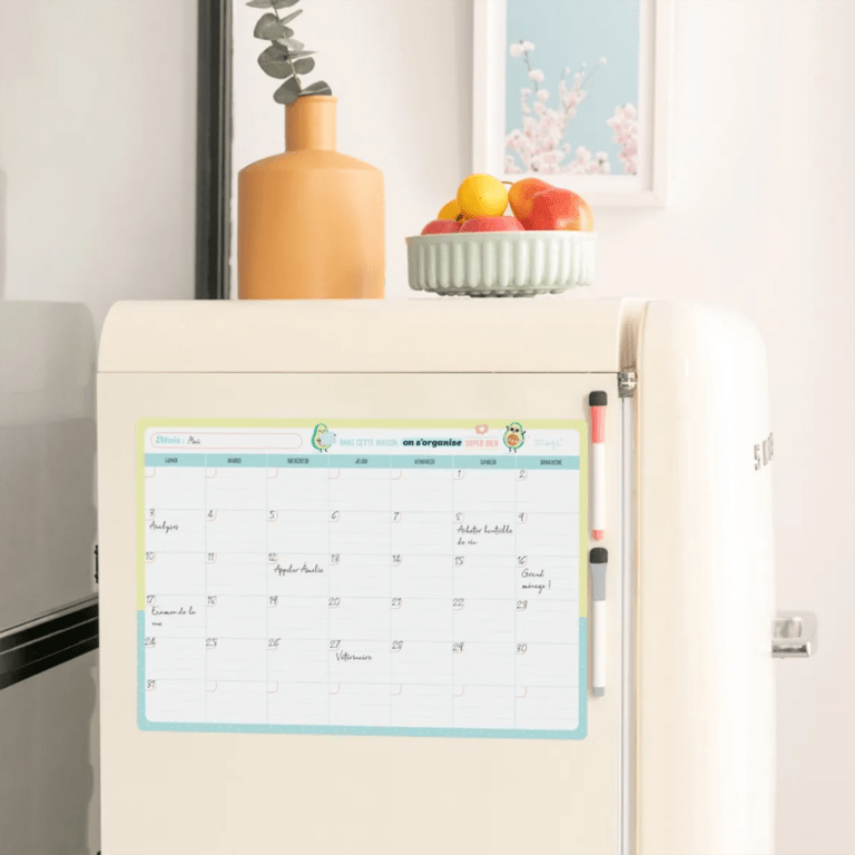 un tableau magnétique avec un planning mensuel, vue de face fixé sur un frigo sur un fond décoré