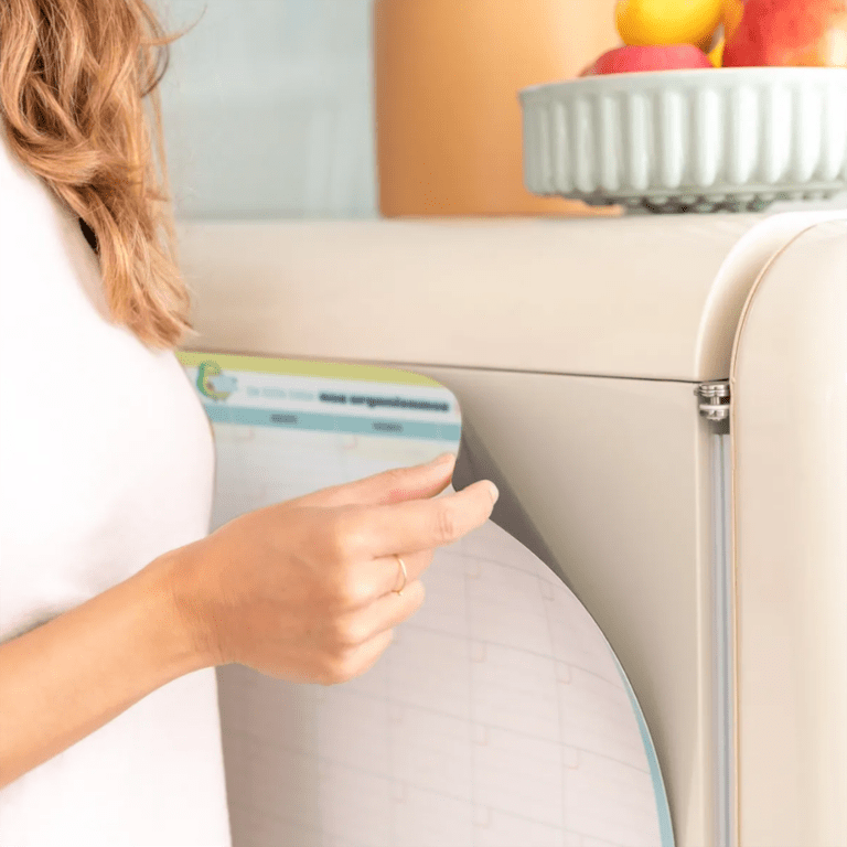un tableau magnétique avec un planning mensuel, vue de face fixé sur un frigo sur un fond décoré
