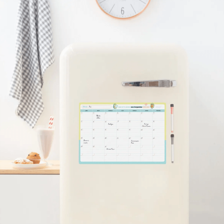 un tableau magnétique avec un planning mensuel, vue de face fixé sur un frigo sur un fond décoré