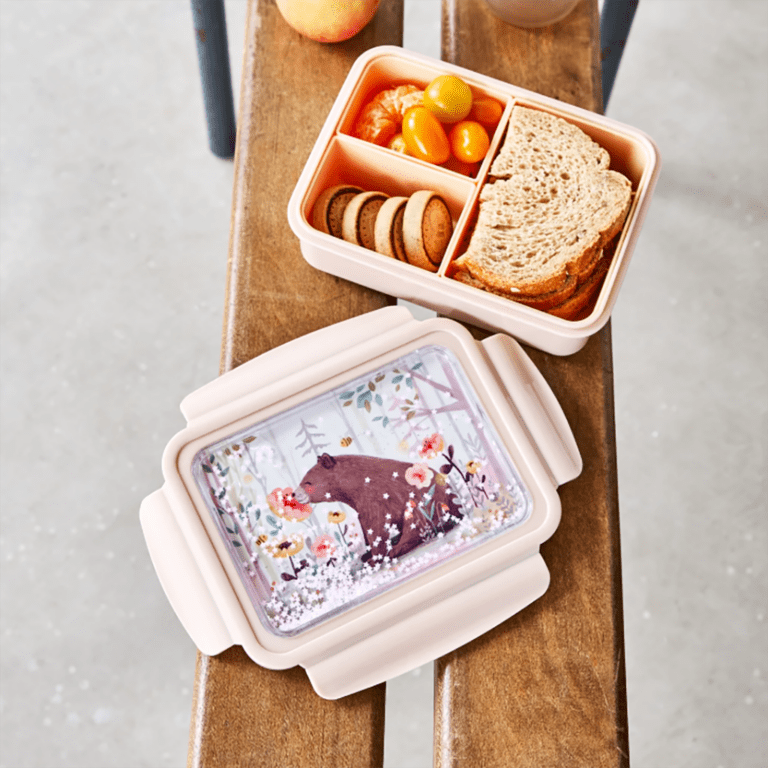 une boîte à repas ours avec un couvercle à paillettes. Il y a trois compartiments amovibles. Vue de face ouverte et utilisée sur un fond décorer