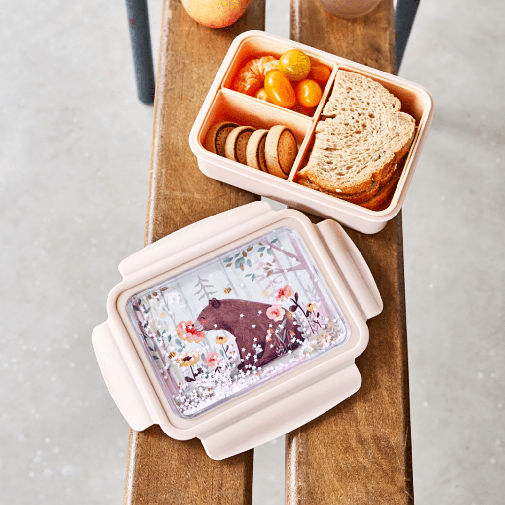 une boîte à repas ours avec un couvercle à paillettes. Il y a trois compartiments amovibles. Vue de face ouverte et utilisée sur un fond décorer