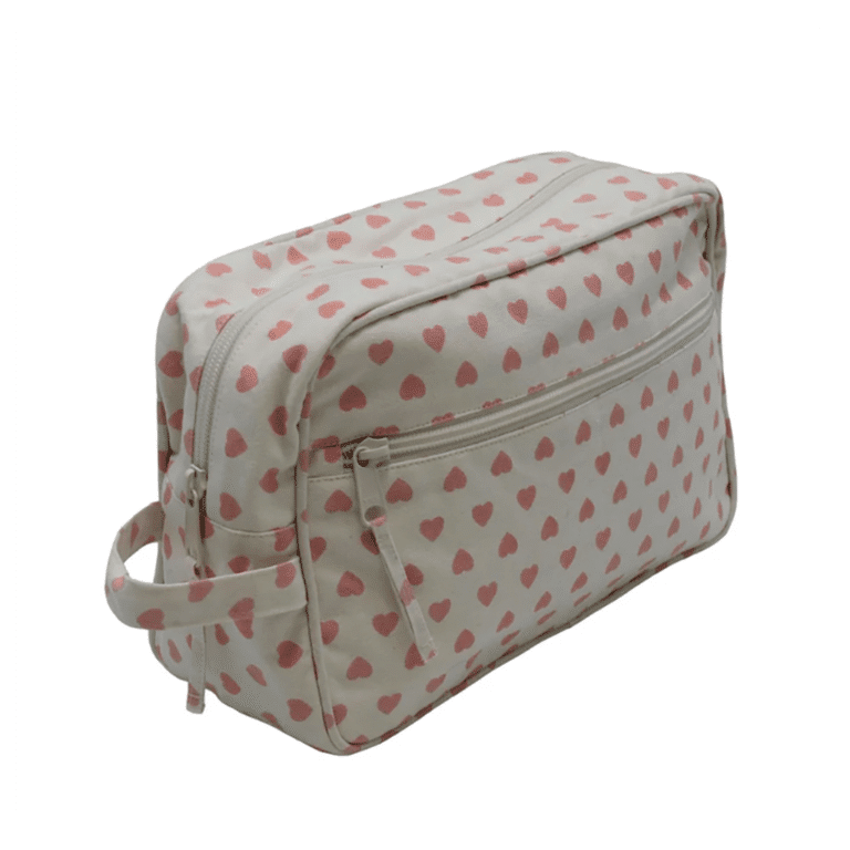 une grande trousse de toilette beige avec des cœurs rose, vue de face sur fond blanc