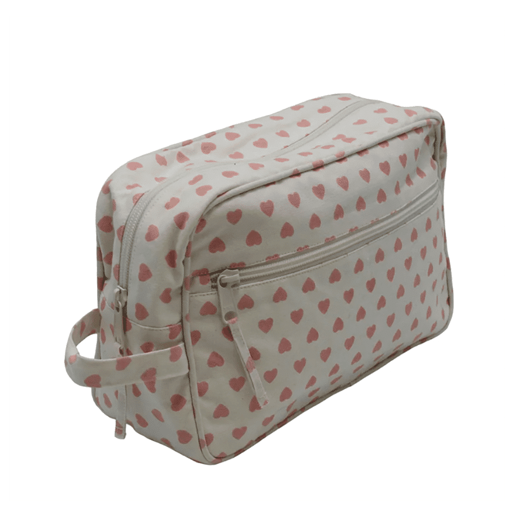 une grande trousse de toilette beige avec des cœurs rose, vue de face sur fond blanc