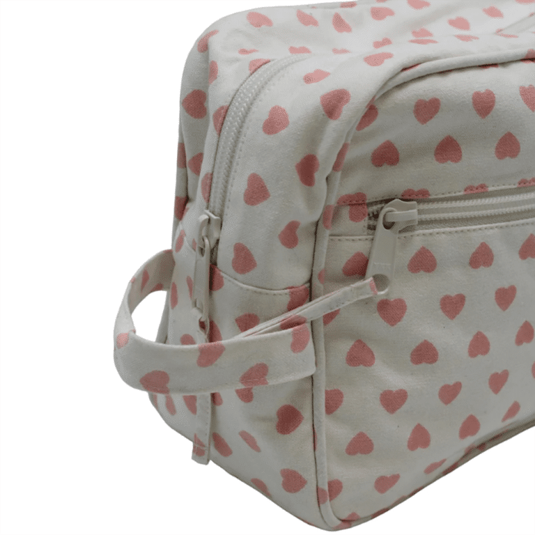 une grande trousse de toilette beige avec des cœurs rose, sur fond blanc