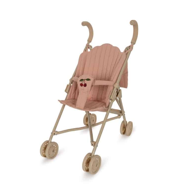 une poussette rose avec une petite cerise Konges Slojd, vue de face sur fond blanc