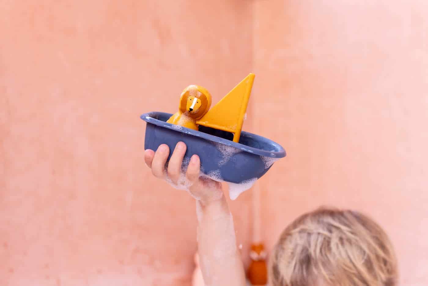 Trixie Baby - jouet de bain voilier Mr.Lion - Vu dans la main d'un enfant sur fond rose