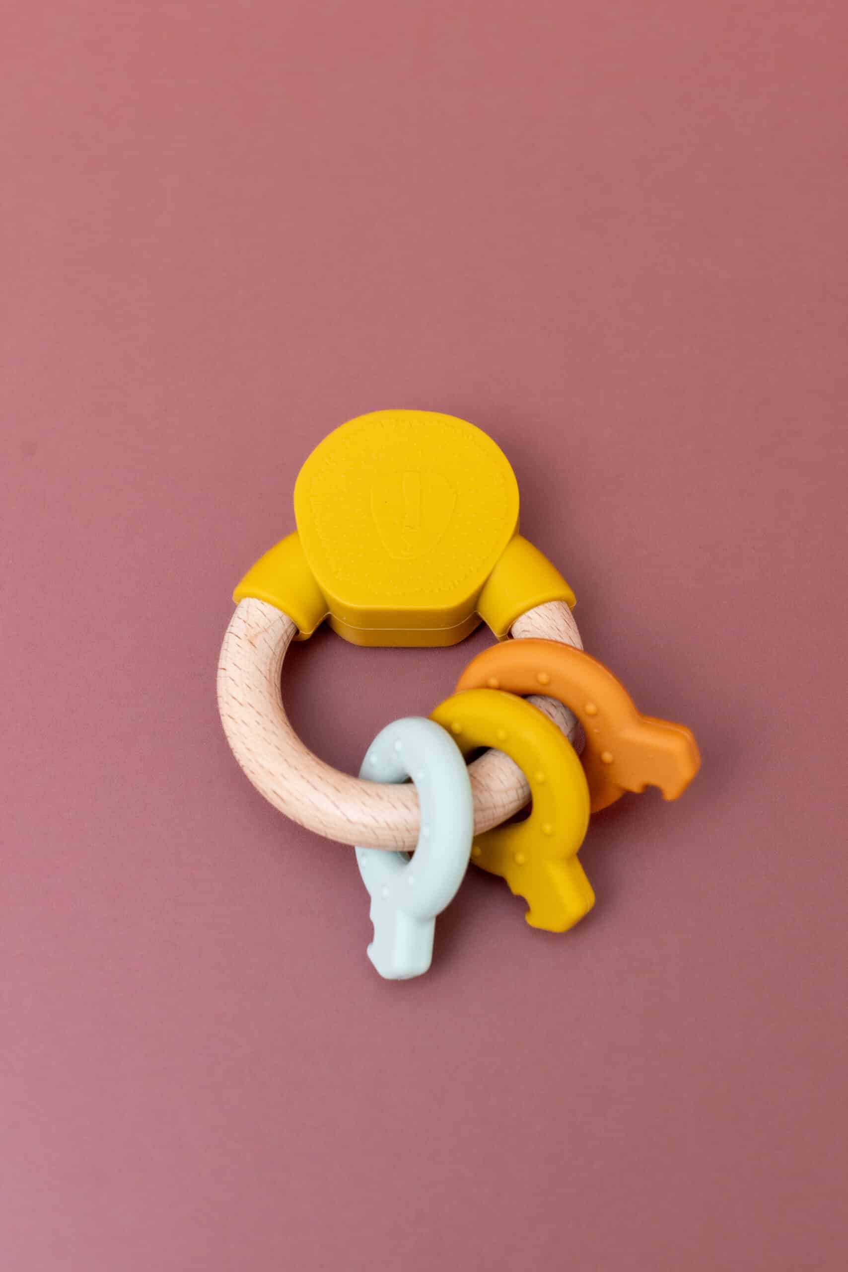 Anneau d’activités en silicone et bois – Mr Lion – Trixie Baby - Vu de face sur fond coloré